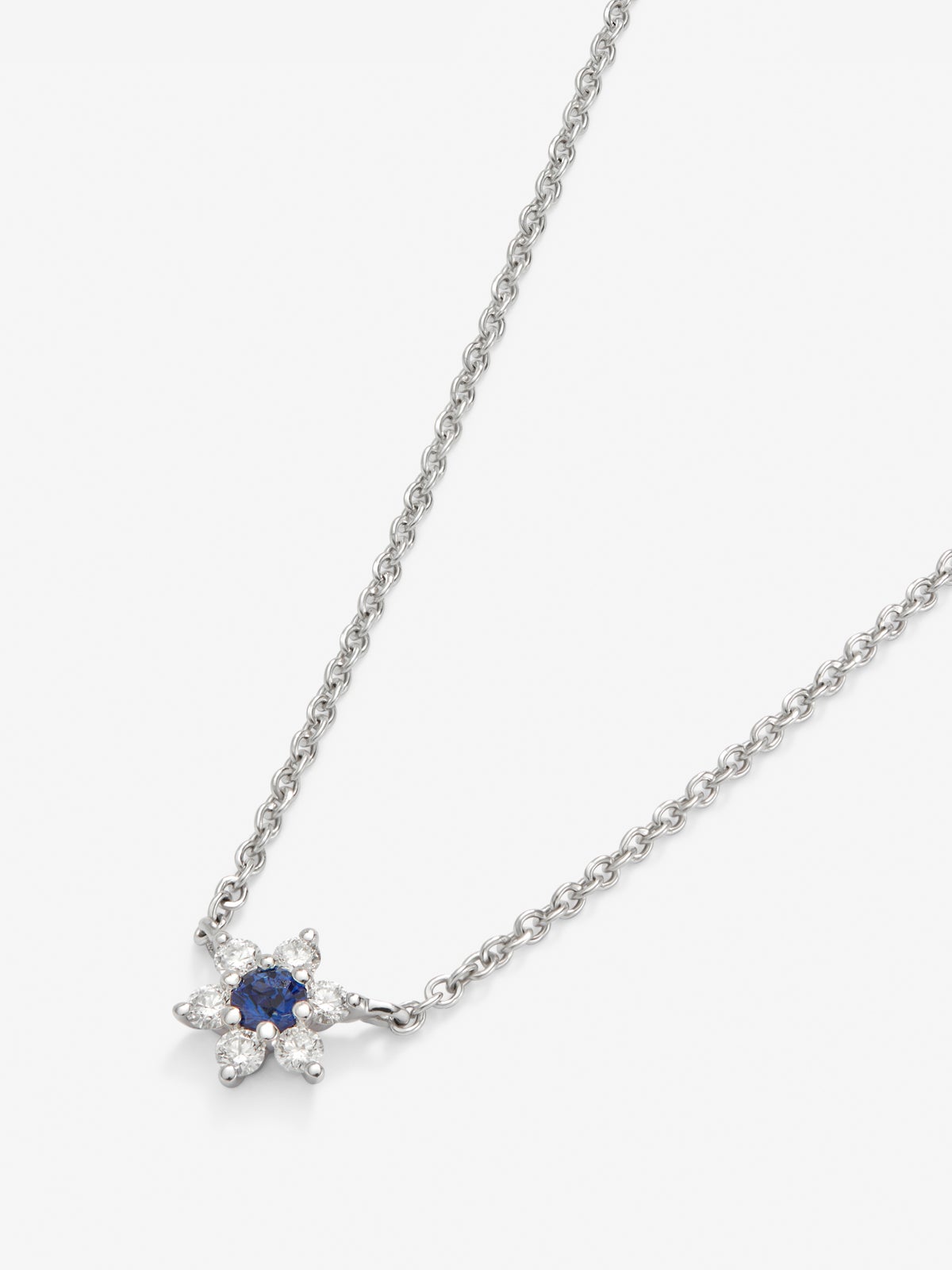 Colgante de oro blanco de 18K con zafiro azul en talla brillante de 0,1 cts y 6 diamantes en talla brillante con un total de 0,12 cts en forma de estrella
