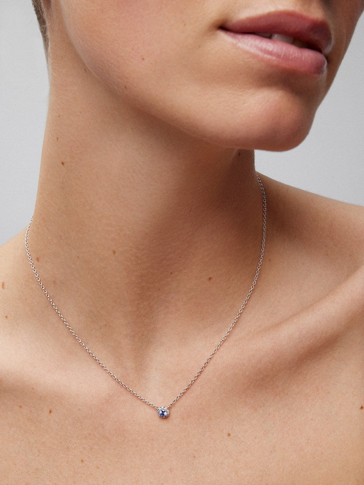 Colgante de oro blanco de 18K con zafiro azul en talla brillante de 0,23 cts y orla de 10 diamantes en talla brillante con un total de 0,07 cts