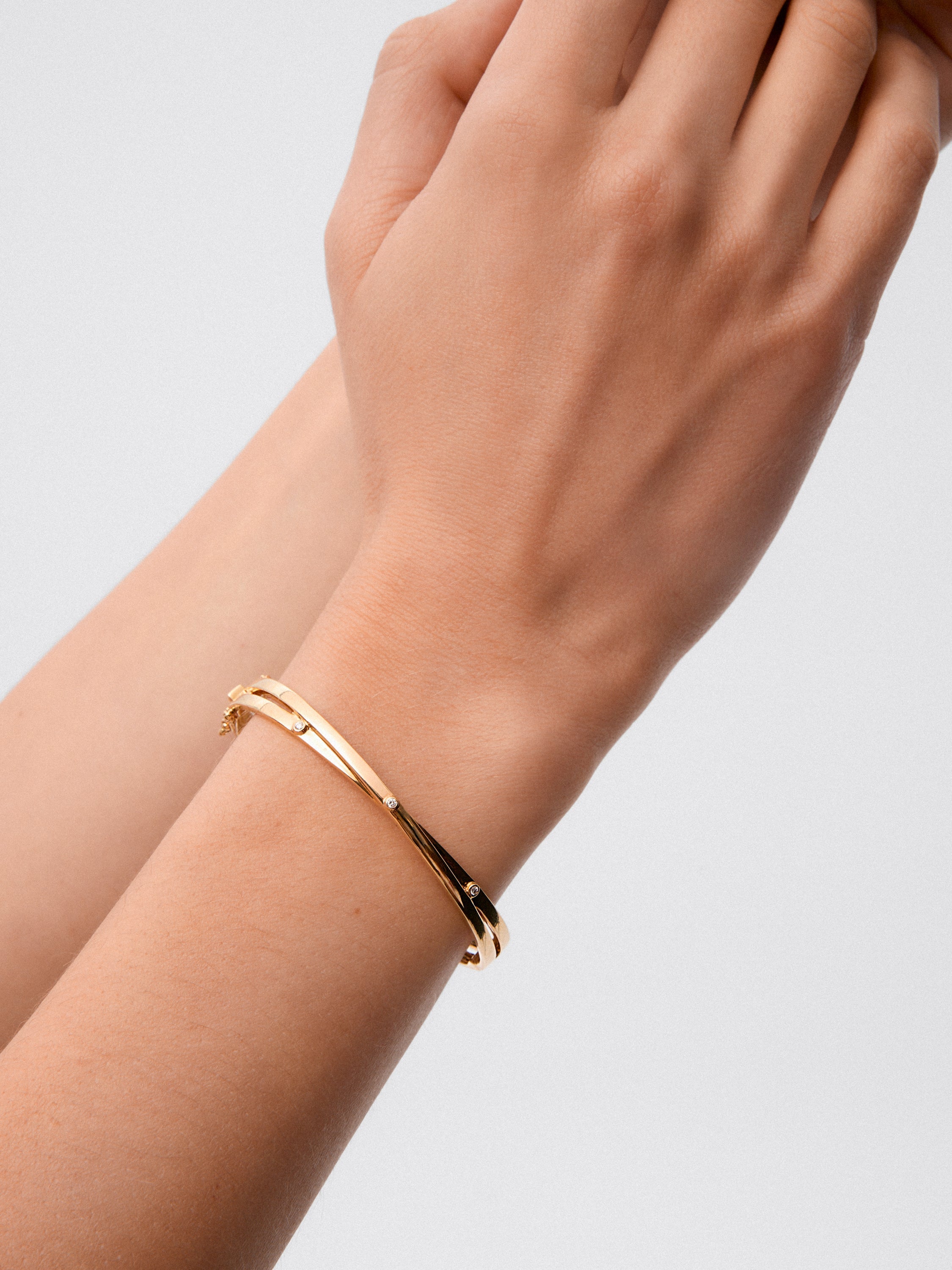 Pulsera rígida cruzada de oro amarillo de 18K con 3 diamantes en talla brillante con un total de 0,04 cts