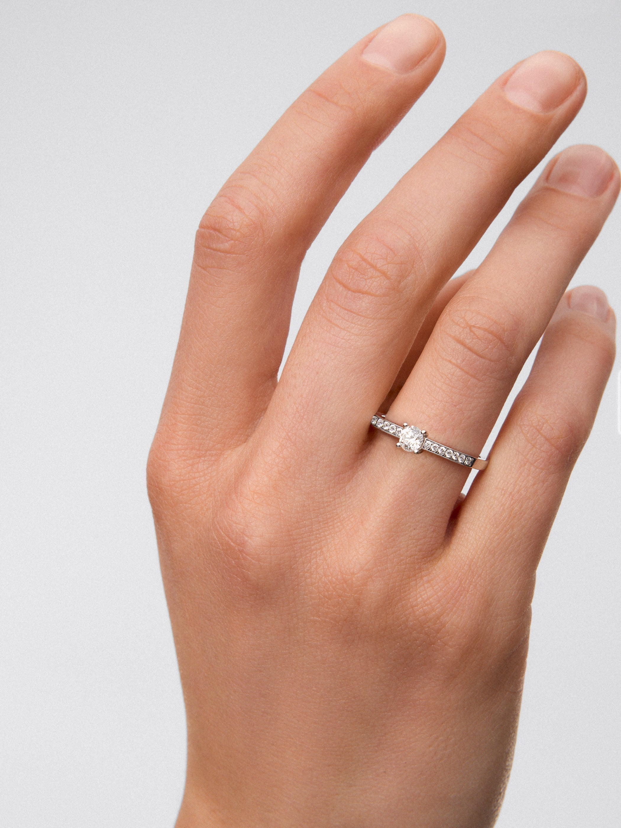 Anillo solitario de oro blanco de 18K con diamante central en talla brillante de 0,3 cts y brazo de 18 diamantes en talla brillante con un total de 0,13 cts