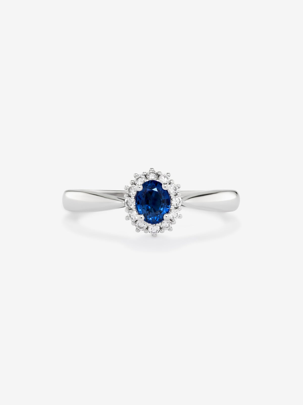 Anillo de oro blanco de 18K con zafiro azul central en talla oval de 0,25 cts y orla de diamantes en talla brillante con un total de 0,18 cts