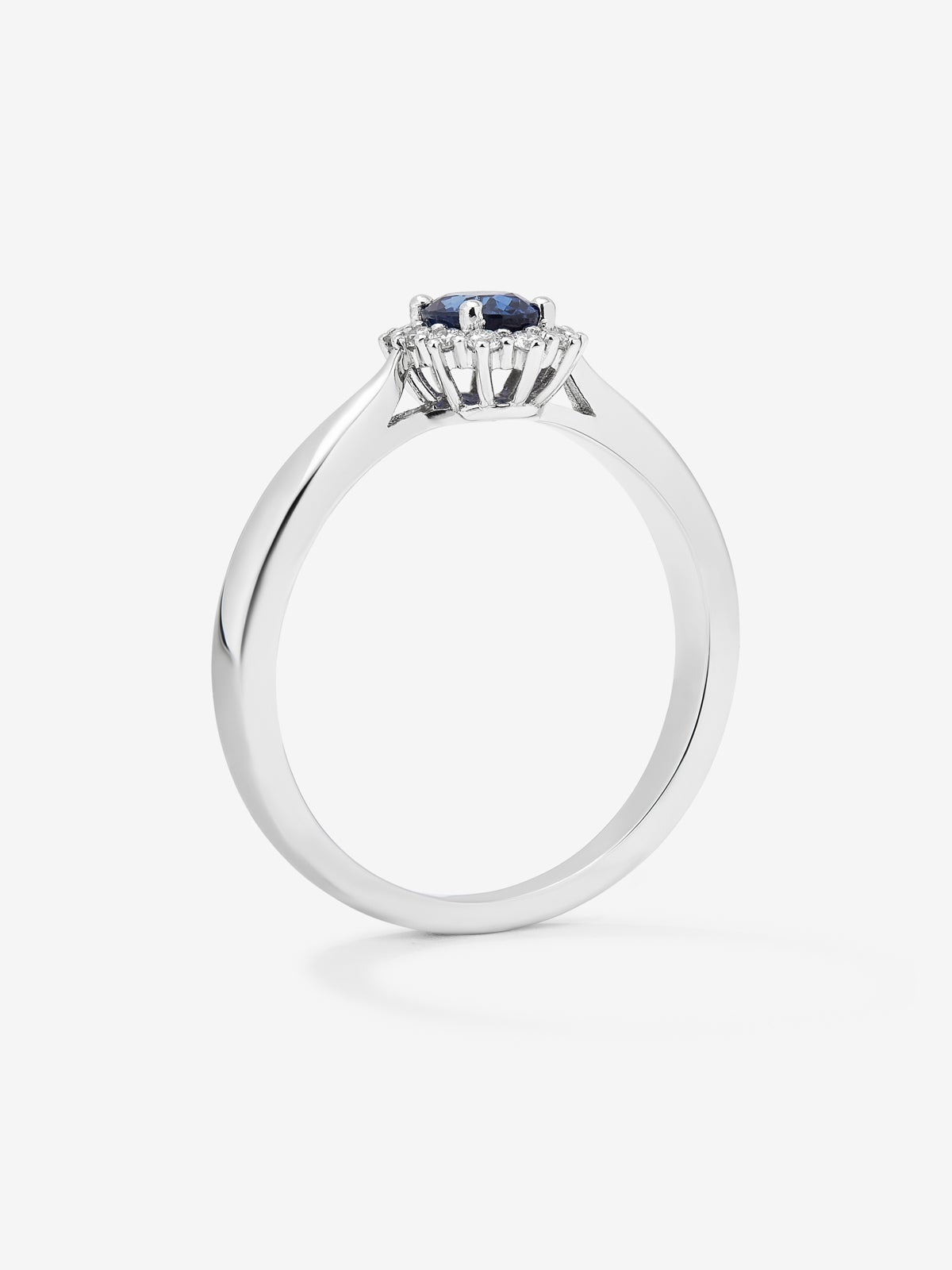 Anillo de oro blanco de 18K con zafiro azul central en talla oval de 0,25 cts y orla de diamantes en talla brillante con un total de 0,18 cts