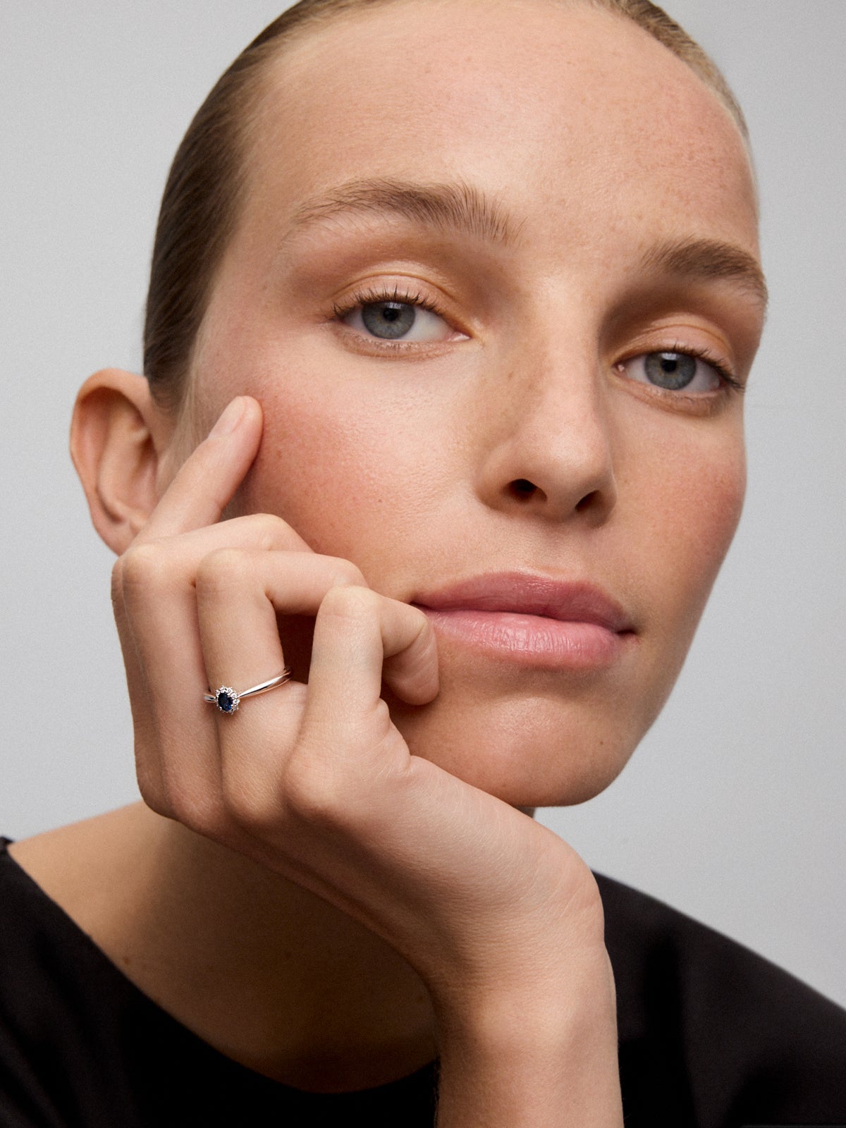 Anillo de oro blanco de 18K con zafiro azul central en talla oval de 0,20 cts y orla de diamantes en talla brillante con un total de 0,10 cts