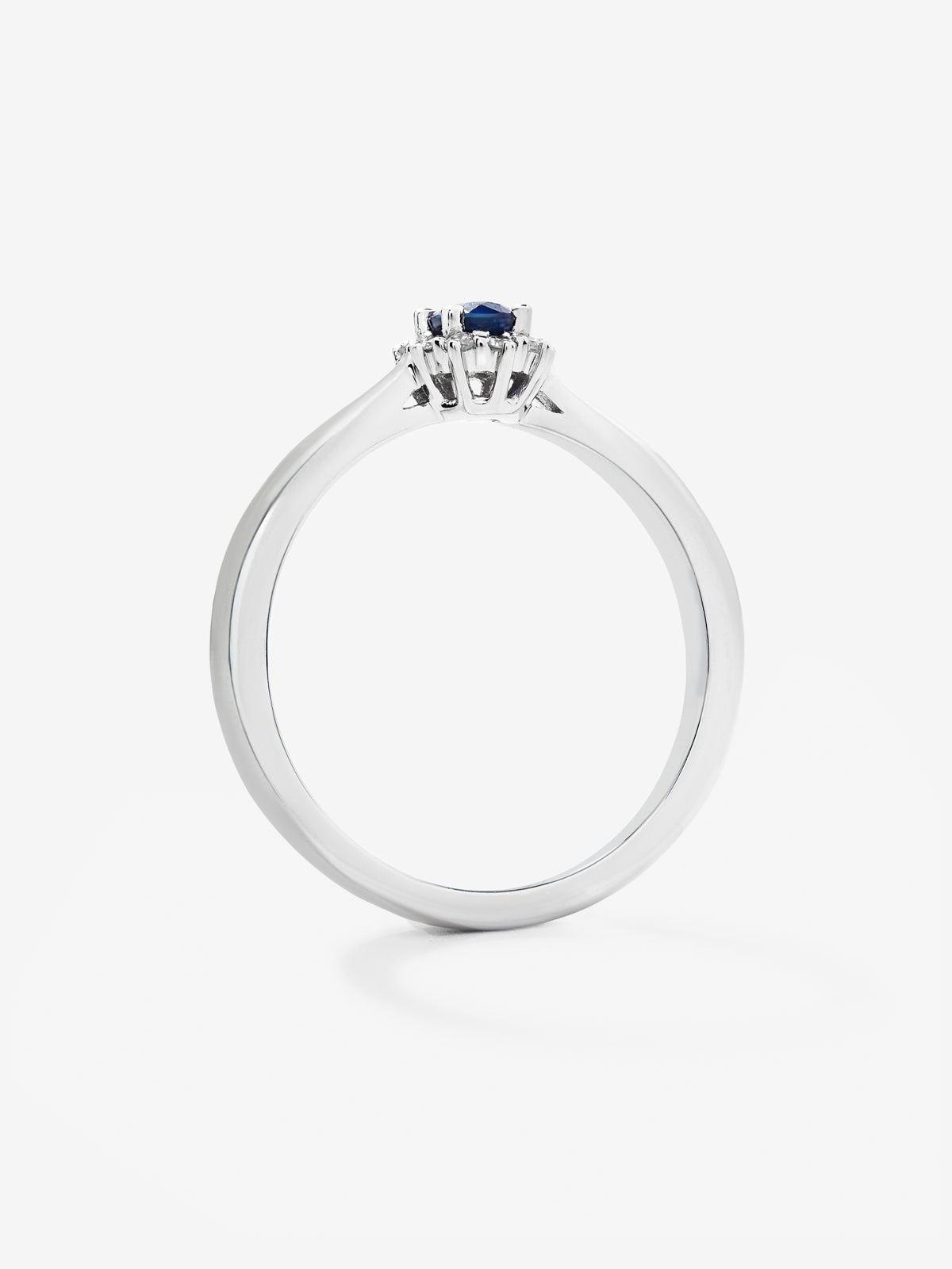 Anillo de oro blanco de 18K con zafiro azul central en talla oval de 0,20 cts y orla de diamantes en talla brillante con un total de 0,10 cts