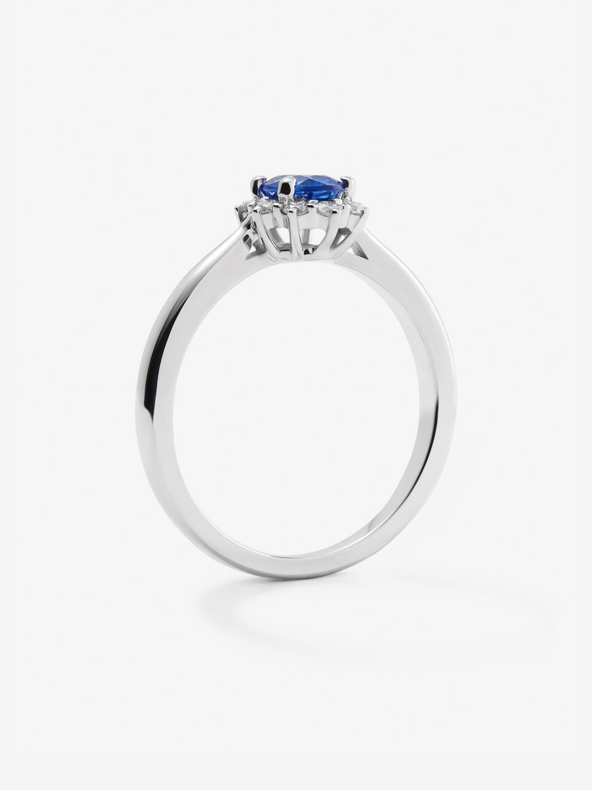 Anillo de oro blanco de 18K con zafiro azul central en talla oval de 0,4 cts y orla de diamantes en talla brillante con un total de 0,25 cts