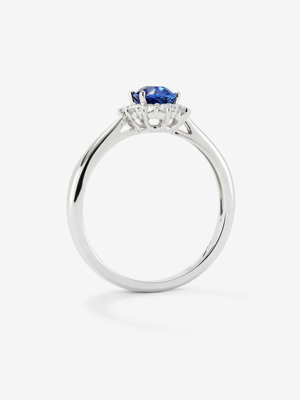 Anillo de oro blanco de 18K con zafiro azul central en talla oval de 0,4 cts y orla de diamantes en talla brillante con un total de 0,25 cts