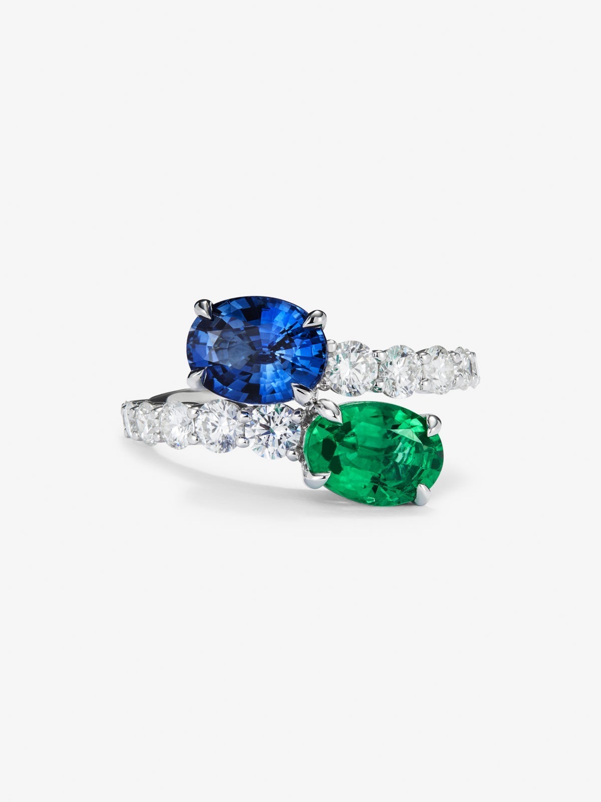 Anillo tú y yo de oro blanco de 18K con zafiro azul en talla oval de 1,75 cts, esmeralda en talla oval de 1,28 cts y 12 diamantes en talla brillante con un total de 0,25 cts