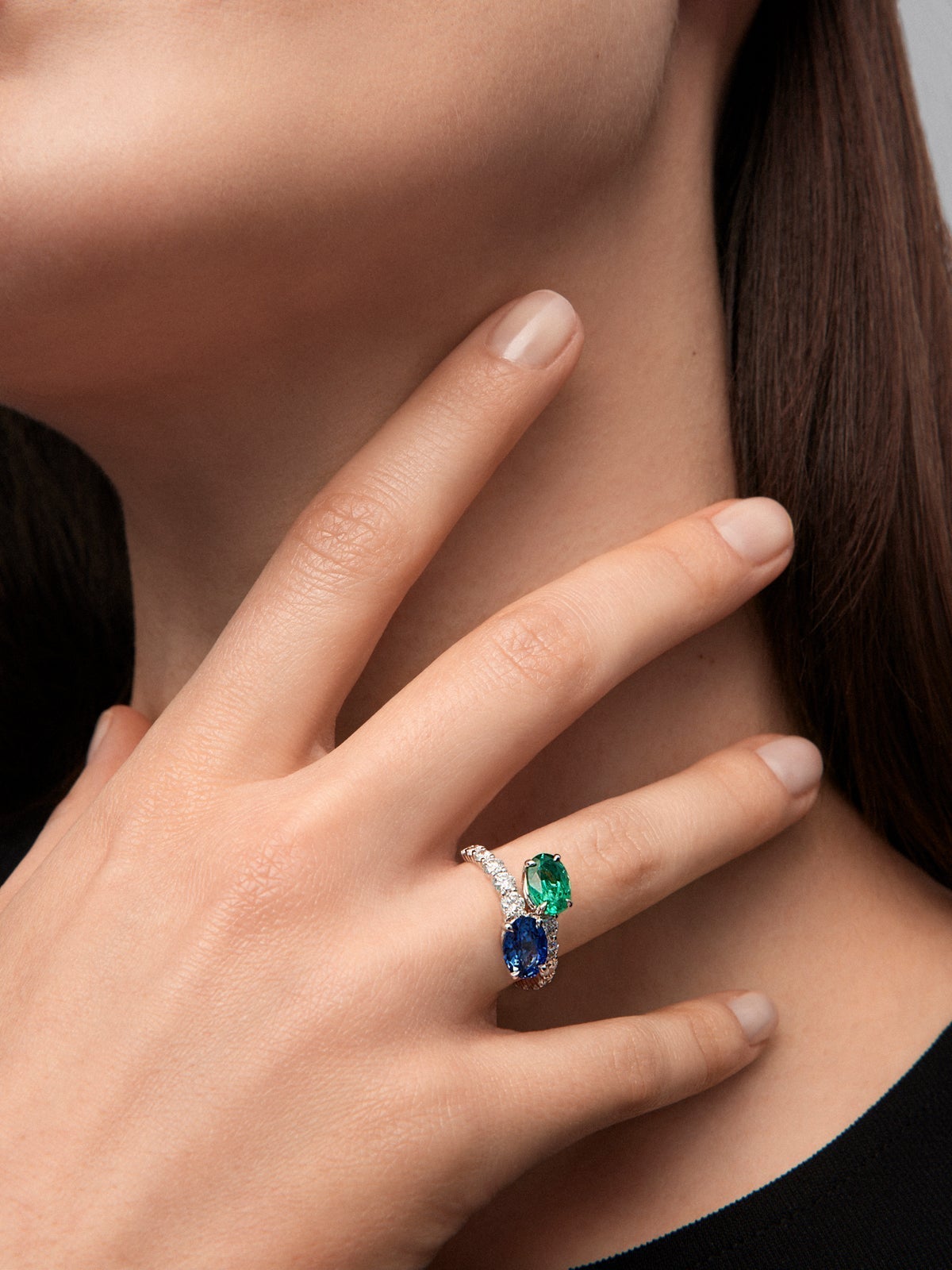 Anillo tú y yo de oro blanco de 18K con zafiro azul en talla oval de 1,75 cts, esmeralda en talla oval de 1,28 cts y 12 diamantes en talla brillante con un total de 0,25 cts